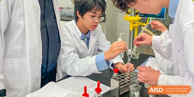 A male student wearing a lab coat carefully using a pipette to conduct a chemical experiment in a laboratory at Wuhan Optics Valley ULINK School.