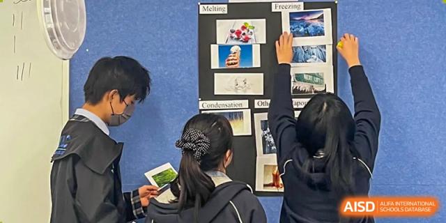 A student pointing to a poster board display about "Melting" and "Freezing" in a science or project-based learning session at Wuhan Optics Valley ULINK School.