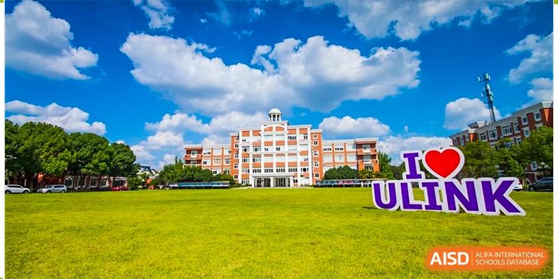 A large, modern red-brick school building with a white columned entrance, set on a vast, well-maintained green lawn at Wuhan Optics Valley ULINK School.