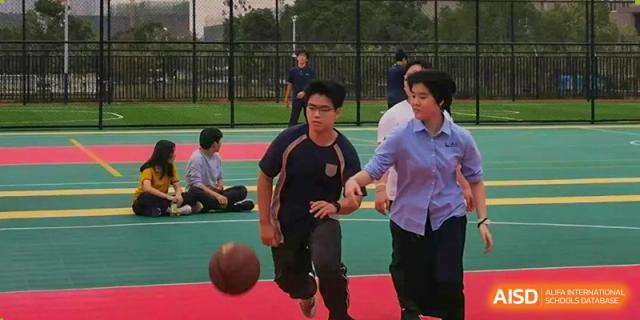 Two male students playing basketball outdoors on a court during a physical education class or break time at Wuhan Optics Valley ULINK School.