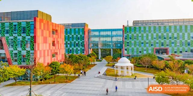 A colorful, modern school building exterior with a red and blue facade and students walking outside at Wuhan Optics Valley ULINK School.
