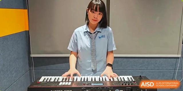 A female student in school uniform smiling while playing a digital keyboard in a music classroom at Wuhan Optics Valley ULINK School.