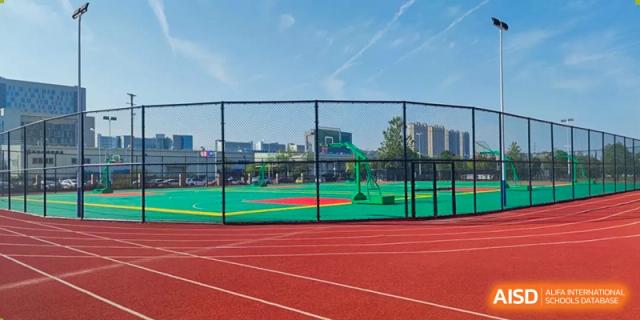 A clear view of the red running track and green sports field bordered by a high fence at Wuhan Optics Valley ULINK School.