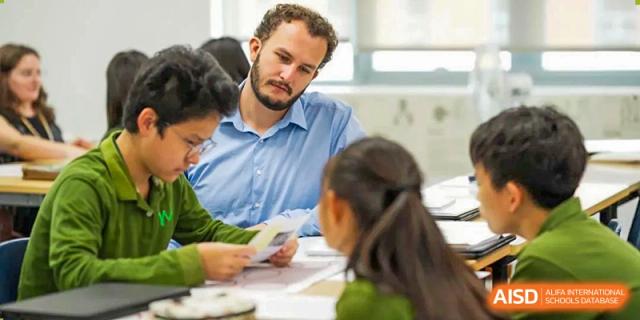 A Wuhan Yangtze International School teacher leans in to help a small group of students seated around a table with a classroom activity.