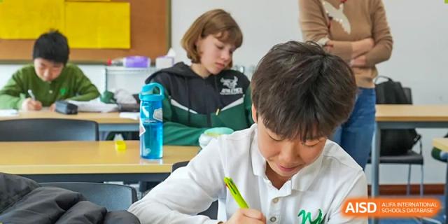 Wuhan Yangtze International School students focused on their individual work at a desk during a class, with one student writing intently.