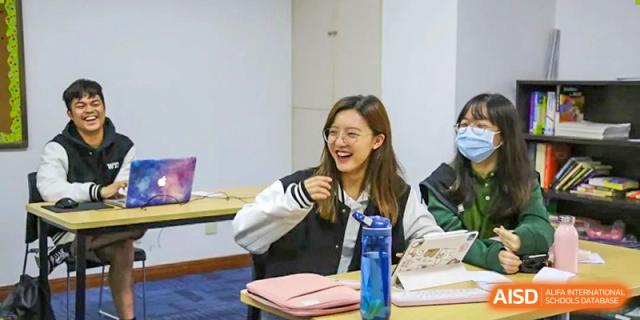 A happy Wuhan Yangtze International School student laughing while seated at a desk with a notebook and water bottle during a class.