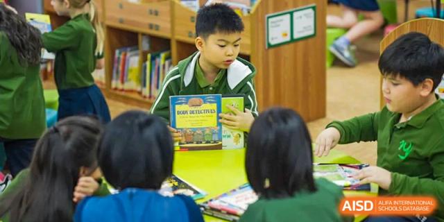 A young Wuhan Yangtze International School student reading a book while sitting on the floor surrounded by bookshelves in the school library.