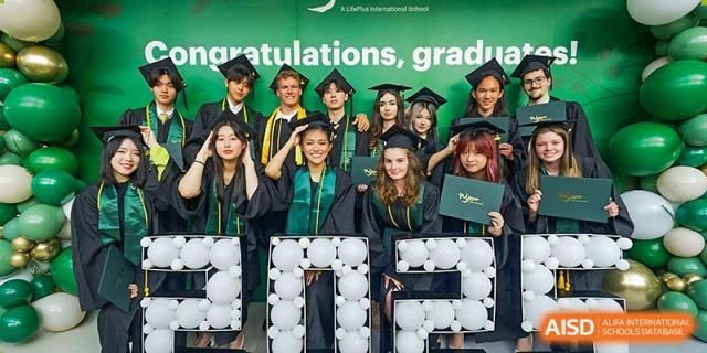A group of diverse Wuhan Yangtze International School high school graduates in caps and gowns smiling for a photo under a "congratulations, grads" banner.