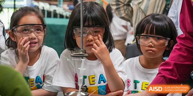 A young Wuhan Yangtze International School female student wearing safety goggles and concentrating on a scientific experiment set up on a table.