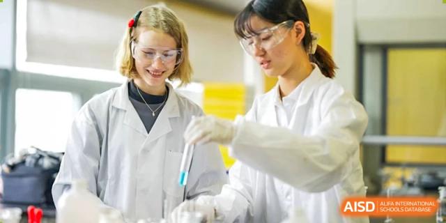 Two Wuhan Yangtze International School students in lab coats and safety glasses carefully working with test tubes in a science lab.