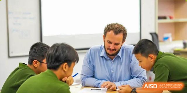 A Wuhan Yangtze International School teacher leans across a table to engage with two students during a discussion or tutoring session.