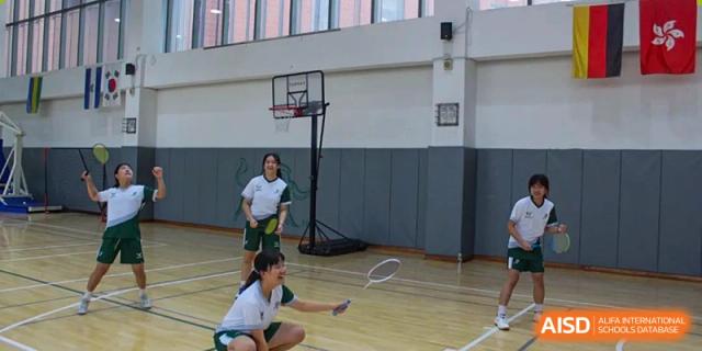 A close-up of a group of Wuhan Yangtze International School students in green and white badminton uniforms posing for a team photo under a banner that says "WATER BUFFALOES."