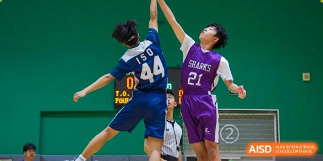 A dynamic shot of a basketball game featuring Wuhan Yangtze International School students, with two players jumping up to contest a shot near the hoop.