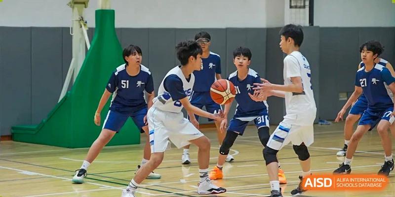 Wuhan Yangtze International School students playing a basketball game, with one student dribbling and others looking on in the background.