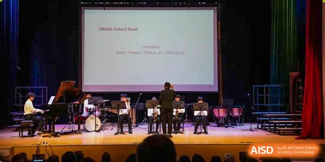 The Wuhan Yangtze International School Middle School Band performing on a stage, with students playing various instruments and a conductor standing with their back to the audience.