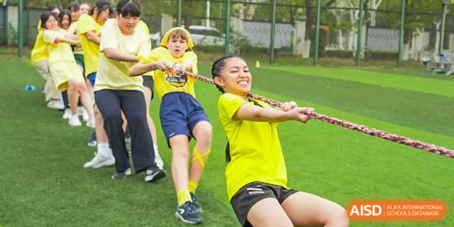 Two Wuhan Yangtze International School students smiling and intensely pulling on a thick rope during a tug-of-war competition.