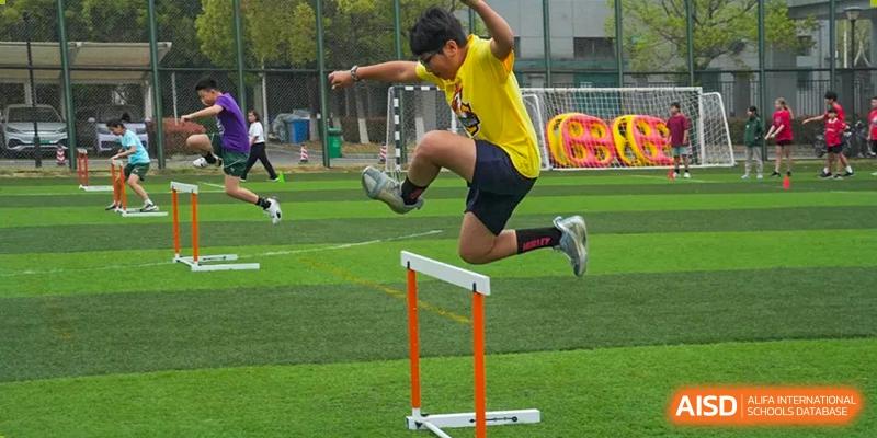 A Wuhan Yangtze International School student in a yellow shirt mid-air as they jump over a low hurdle on an outdoor track and field.