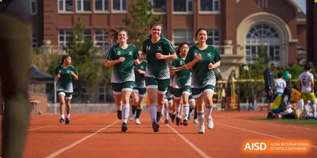A group of Wuhan Yangtze International School female athletes in green uniforms running together on a bright red track.