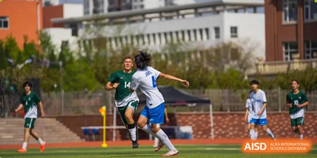 A Wuhan Yangtze International School student in a white and blue jersey kicking a soccer ball while running on a turf field.