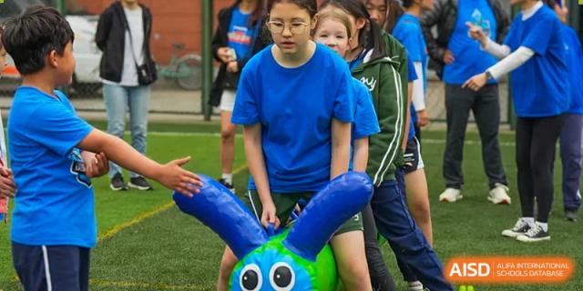A close-up of a Wuhan Yangtze International School student in a blue shirt participating in an indoor game with a large, inflatable blue and green object.