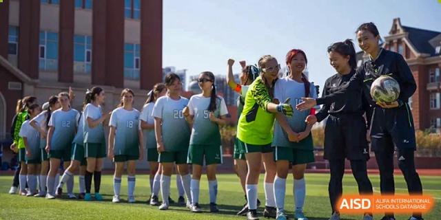A group of Wuhan Yangtze International School students and athletes cheering with their hands raised in a sunny outdoor setting.