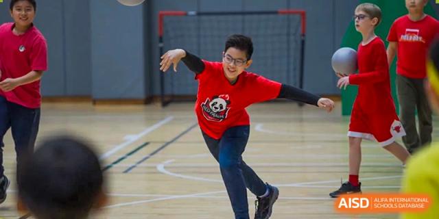 A Wuhan Yangtze International School student in a red shirt with a panda graphic performing a dynamic move on an indoor gymnasium floor.