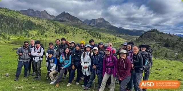 A group of Wuhan Yangtze International School students and adults posing on a trail during a mountain hiking trip under an overcast sky.