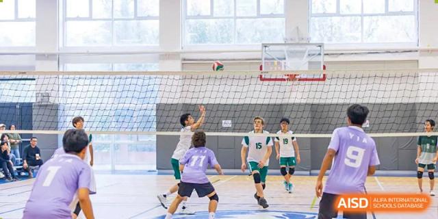 Wuhan Yangtze International School students in green and white uniforms playing an intense game of volleyball on an indoor court.