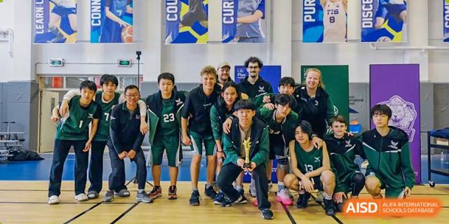 A Wuhan Yangtze International School boys' sports team, all wearing dark green jerseys, posing proudly with a championship trophy indoors.