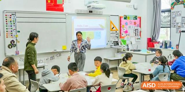 A teacher interacting with a group of primary or middle school students gathered around a whiteboard in a bright classroom at Wuxi Dipont School of Arts and Science.