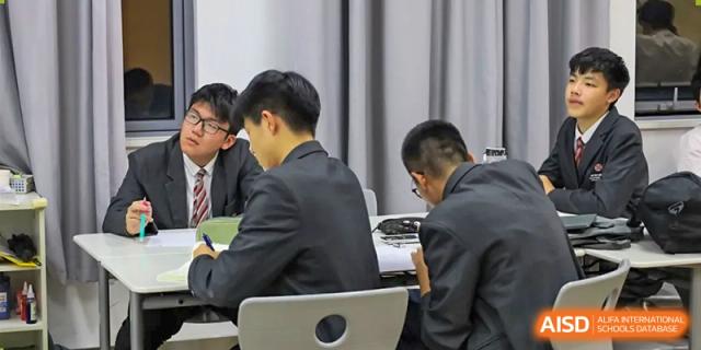 Two high school students in dark suits and ties focused on their work or exams at individual desks at Wuxi Dipont School of Arts and Science.