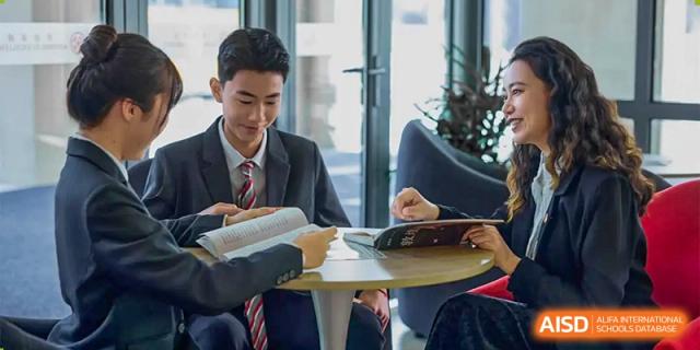 Two high school students in school uniforms studying together at a round table in a modern, well-lit study area at Wuxi Dipont School of Arts and Science.