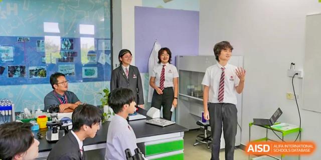 A small group of high school students in uniform standing in a science classroom, possibly engaged in a discussion or experiment setup, at Wuxi Dipont School of Arts and Science.