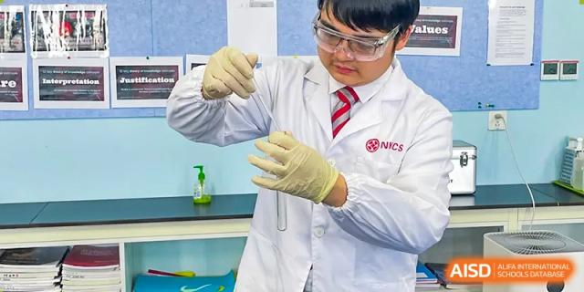 A student in a lab coat and safety glasses holding a test tube during a science experiment in the laboratory at Wuxi Dipont School of Arts and Science.