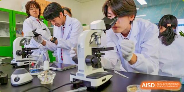 A close-up of students in lab coats working with a microscope during a science class at Wuxi Dipont School of Arts and Science.