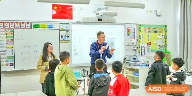 An enthusiastic male teacher instructing a group of young students in a primary classroom using an interactive whiteboard at Wuxi Dipont School of Arts and Science.