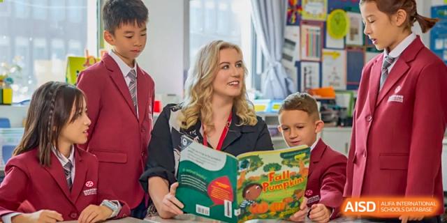 A smiling female teacher reading a picture book to several younger students in a library or classroom setting at Wuxi Dipont School of Arts and Science.