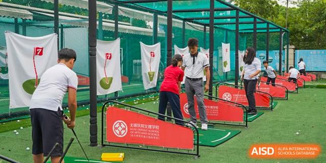 Two students, one in a white shirt and one in a red shirt, practicing golf swings in an outdoor practice cage under the supervision of an instructor at Wuxi Dipont School of Arts and Science.