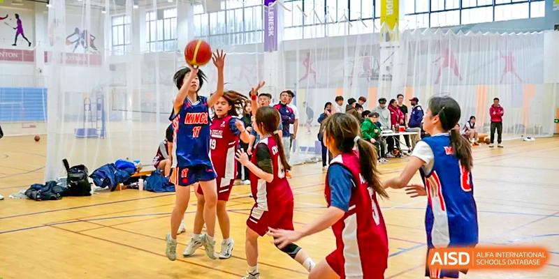 A group of young students in red and blue jerseys playing basketball in a brightly lit indoor court at Wuxi Dipont School of Arts and Science.