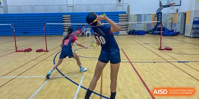 A young girl in a dark blue sports uniform playing badminton in an indoor court at Wuxi Dipont School of Arts and Science.