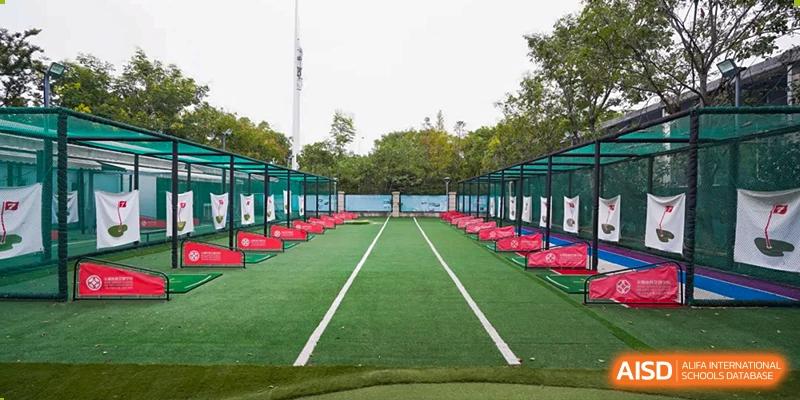 A wide shot of a green outdoor sports field with running track lanes and a covered seating area at Wuxi Dipont School of Arts and Science.