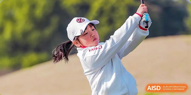 A close-up of a young girl in a white hat and shirt focused on a golf swing outdoors at Wuxi Dipont School of Arts and Science.