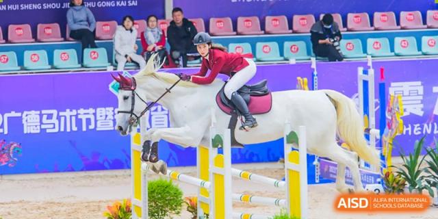 A student on a white horse jumping over an obstacle in an equestrian competition at Wuxi Dipont School of Arts and Science.
