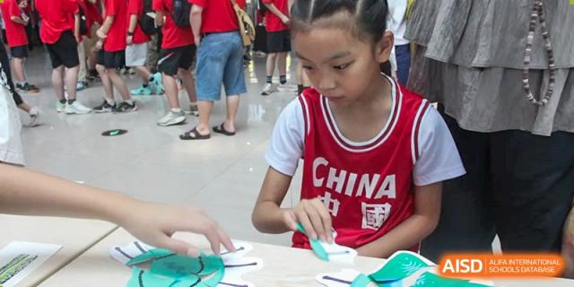 A young student in a red and white jersey focused on a hands-on activity, possibly a craft or science experiment, outdoors at Wuxi Dipont School of Arts and Science.
