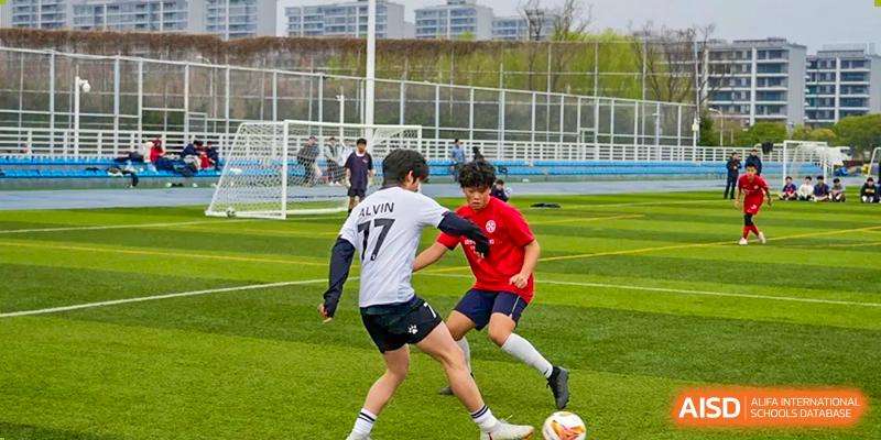 Two male students playing soccer on a green turf field during an outdoor sports session at Wuxi Dipont School of Arts and Science.