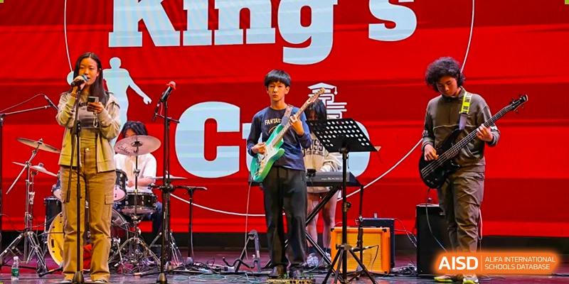 A male student playing an electric guitar with a keyboard player and a large banner in the background on an outdoor stage at Wuxi Dipont School of Arts and Science.