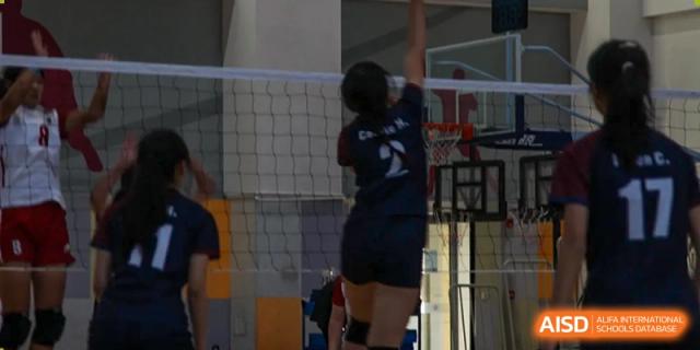 A student jumping to block a ball near the net during an indoor volleyball game at Wuxi Dipont School of Arts and Science.