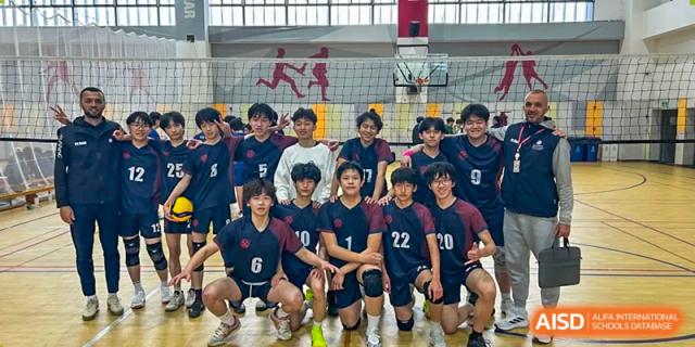 A high school boys' volleyball team, wearing dark uniforms and knee pads, kneeling and posing for a group photo in the gymnasium at Wuxi Dipont School of Arts and Science.
