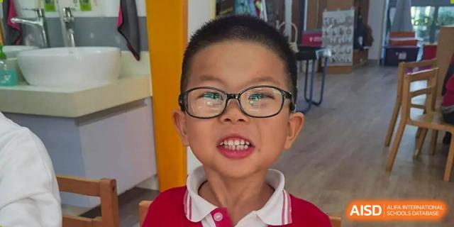 A close-up portrait of a young male student in glasses and a red polo shirt smiling at the camera at Wuxi Dipont School of Arts and Science.