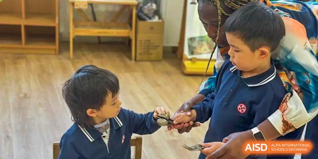 An adult helping a young student hold a small animal, possibly a chick or reptile, during a learning activity at Wuxi Dipont School of Arts and Science.